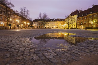 Poland, Masovia, Warsaw, Illuminated town square reflecting in puddle at night