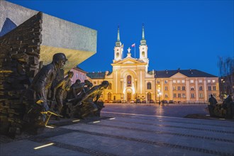 Poland, Masovia, Warsaw, Town square with World War II monument and illuminated cathedral