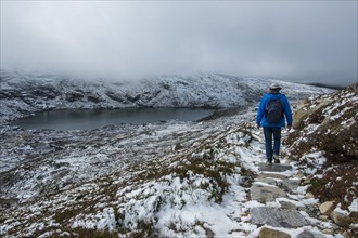 Australia, New South Wales, Woman hiking on snowy trail by lake at Charlotte Pass in Kosciuszko National Park