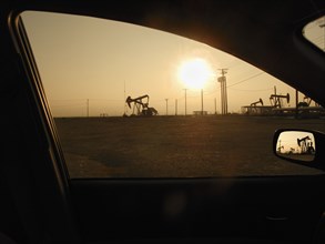 Silhouette of pump jacks in oil field at sunset seen from car