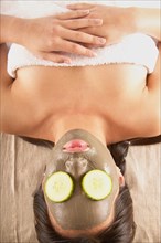 Woman with mud mask and cucumbers on face