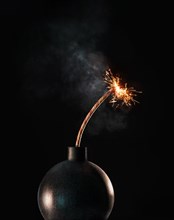 Black bomb with lit fuse against black background
