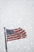 Torn American flag on flag pole with falling snow