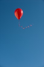 Red balloon with ribbon flying against blue sky