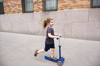 Girl riding push scooter on sidewalk