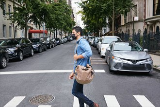 Man in face mask crossing street in city
