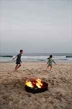 Boy and girl playing on beach near bonfire