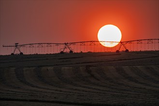 Irrigation equipment in field against setting sun