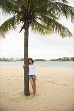 Smiling woman hugging palm tree on tropical beach