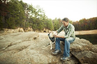 Man petting dog on rocks near lake