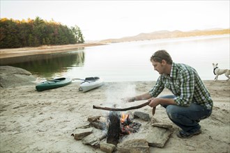 Man building campfire at lake