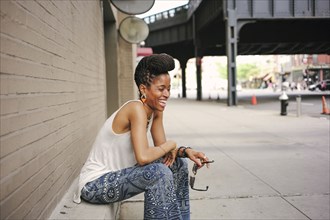 African American woman with braids sitting on ledge and laughing