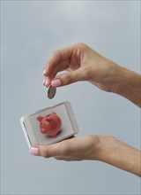 Caucasian woman depositing coin in cell phone piggy bank