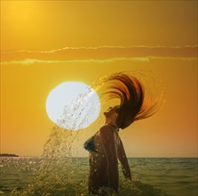 Caucasian woman tossing hair in ocean under sunset sky