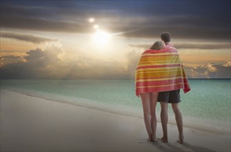Caucasian couple wrapped in towel admiring sunset on beach