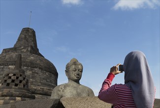 Tourist photographing Buddha statue on Temple of Borobudur