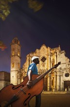 Hispanic musician carrying upright bass near church