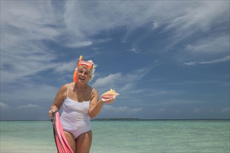 Older Caucasian woman holding conch shell on beach
