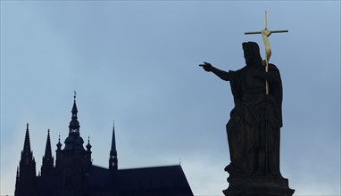 Silhouette of statue and crucifix by church spires