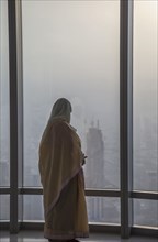 Asian woman at window admiring Dubai cityscape