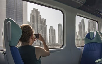 Caucasian woman photographing Dubai cityscape on train