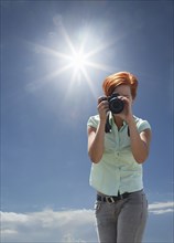 Caucasian woman photographing under blue sky