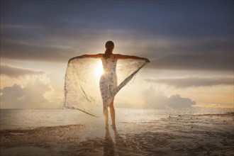 Caucasian woman holding fabric on beach at sunset