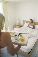 Caucasian woman serving man breakfast in bed