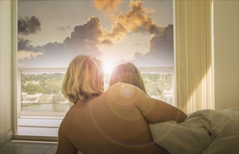 Caucasian couple in bed watching sunset at window