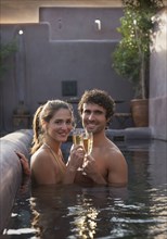 Smiling Caucasian couple toasting with champagne in swimming pool