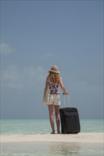 Caucasian woman holding suitcase on ocean beach