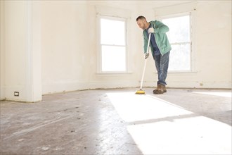 Mixed race man sweeping floor of new home