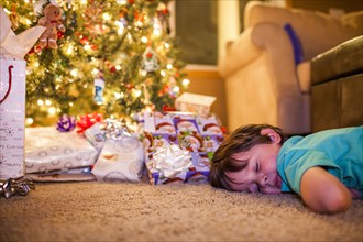 Caucasian boy sleeping by Christmas gifts