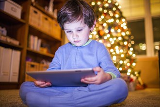 Caucasian boy using digital tablet by Christmas tree