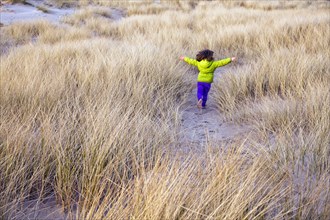 Caucasian girl running in grassy sand dune