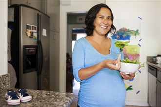 Pregnant Hispanic woman eating salad in kitchen
