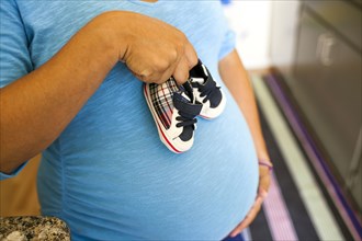 Pregnant Hispanic woman holding baby shoes