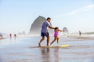Caucasian father and daughter playing in surf on beach