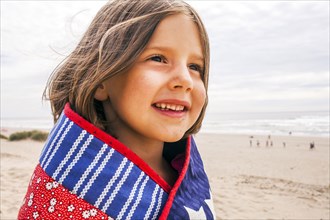 Caucasian girl wrapped in blanket on beach