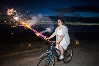Woman holding fireworks on bicycle at night
