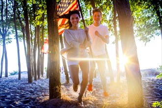 Caucasian couple carrying American flag in trees on beach