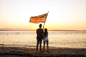 Caucasian couple holding American flag on beach