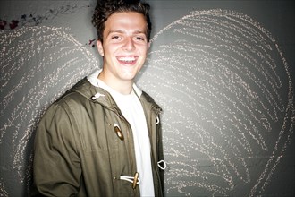 Caucasian man smiling near chalk heart on wall