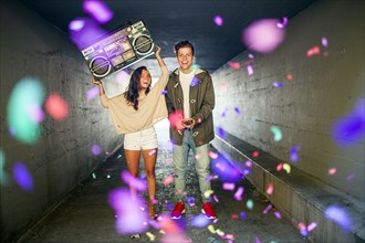 Caucasian couple carrying boom box and throwing confetti in tunnel