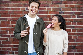 Caucasian couple eating ice cream near red brick wall