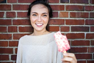 Caucasian woman eating ice cream near red brick wall