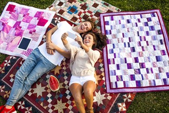Caucasian couple taking selfie on blankets in park