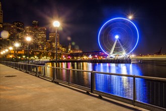 Illuminated ferris wheel on urban waterfront at night