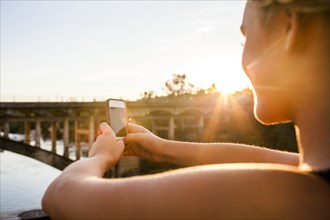 Caucasian teenage girl taking cell phone photograph of bridge