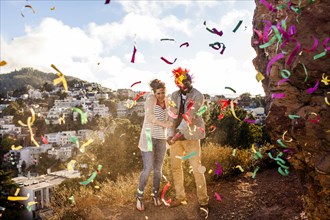 Couple throwing confetti on hill overlooking cityscape